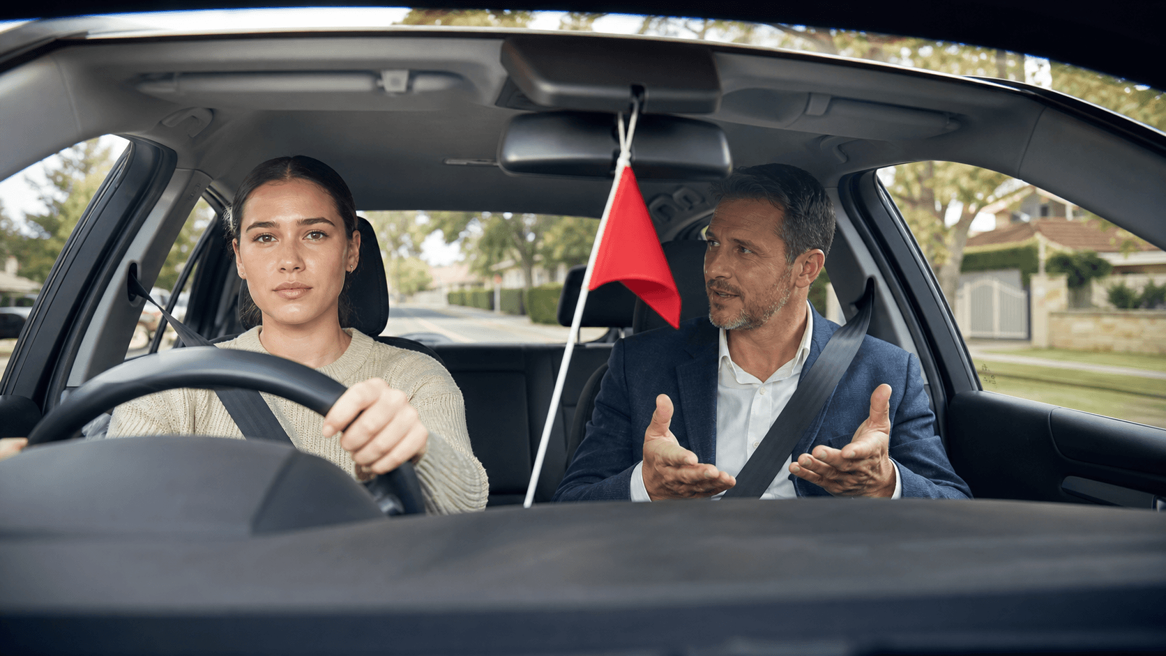 An anxious learner sits in a parked car while a stern instructor points beside Sydney traffic.