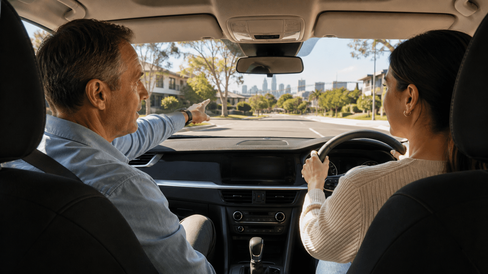 Instructor and learner sit in a modern car, viewed through the windshield against a bright Sydney street.